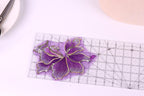 a purple flower-shaped object placed on a transparent ruler, which is placed on a white surface.