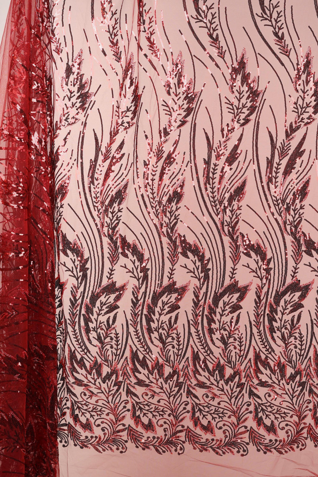 a close-up view of a fabric with a floral pattern in shades of red and black. The pattern consists of various leaf-like shapes and lines, creating a visually striking and intricate design. The fabric appears to be made of a material with a shimmering or sequined texture, adding a touch of elegance and sophistication to the overall appearance.
