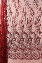 a close-up view of a fabric with a floral pattern in shades of red and black. The pattern consists of various leaf-like shapes and lines, creating a visually striking and intricate design. The fabric appears to be made of a material with a shimmering or sequined texture, adding a touch of elegance and sophistication to the overall appearance.