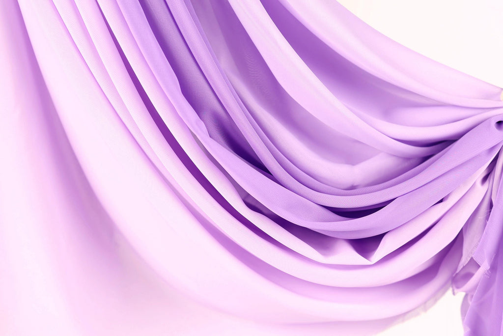 The image is a close-up of a soft, flowing purple fabric, possibly a curtain or garment. The fabric has a smooth, silky texture and is draped in a way that creates a sense of movement and elegance.