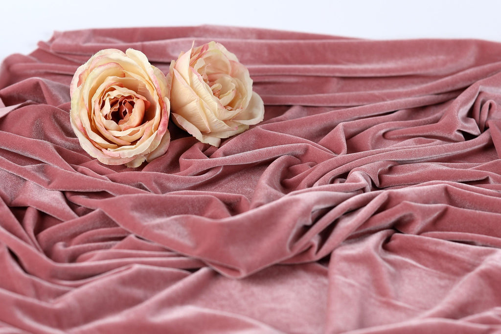 Two light pink roses resting on a crumpled pink fabric.