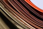 a close-up view of a collection of colorful, shiny fabrics or materials, with a gradient of colors ranging from dark brown to light brown. The fabrics appear to be folded or draped in a way that creates a visually striking and textured effect.