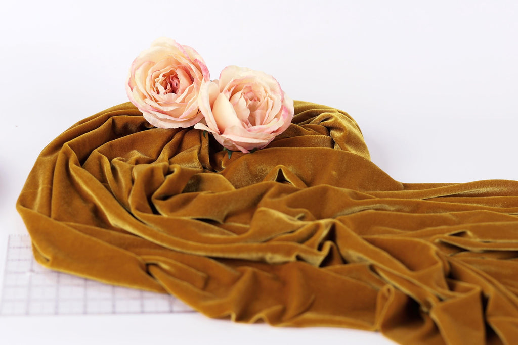 two pink roses resting on a crumpled, golden fabric, which appears to be a piece of velvet or a similar material.