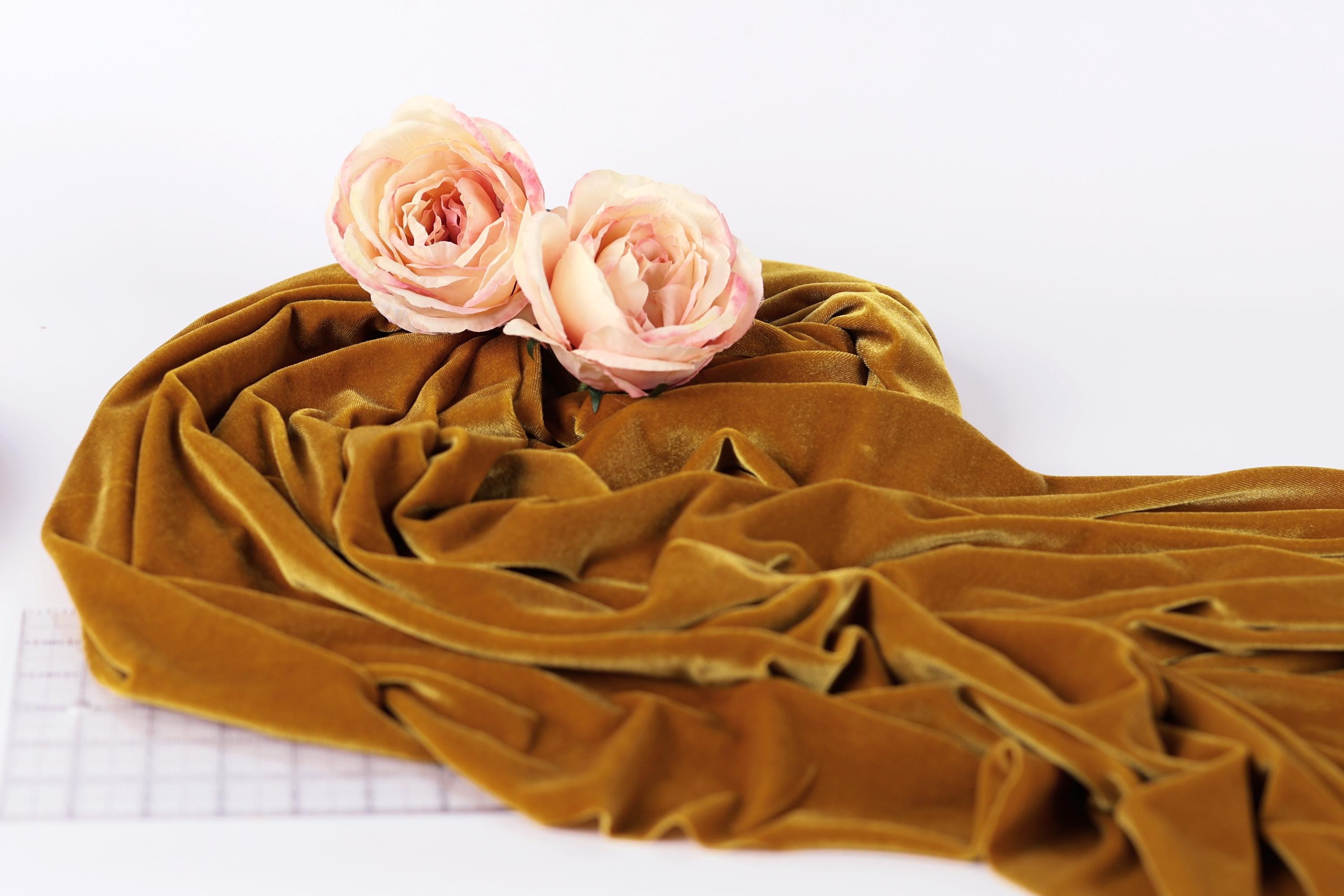 two pink roses resting on a crumpled, golden fabric, which appears to be a piece of velvet or a similar material.