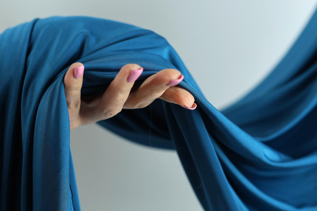 A hand with painted fingernails is holding a blue fabric, which appears to be a piece of clothing or textile.