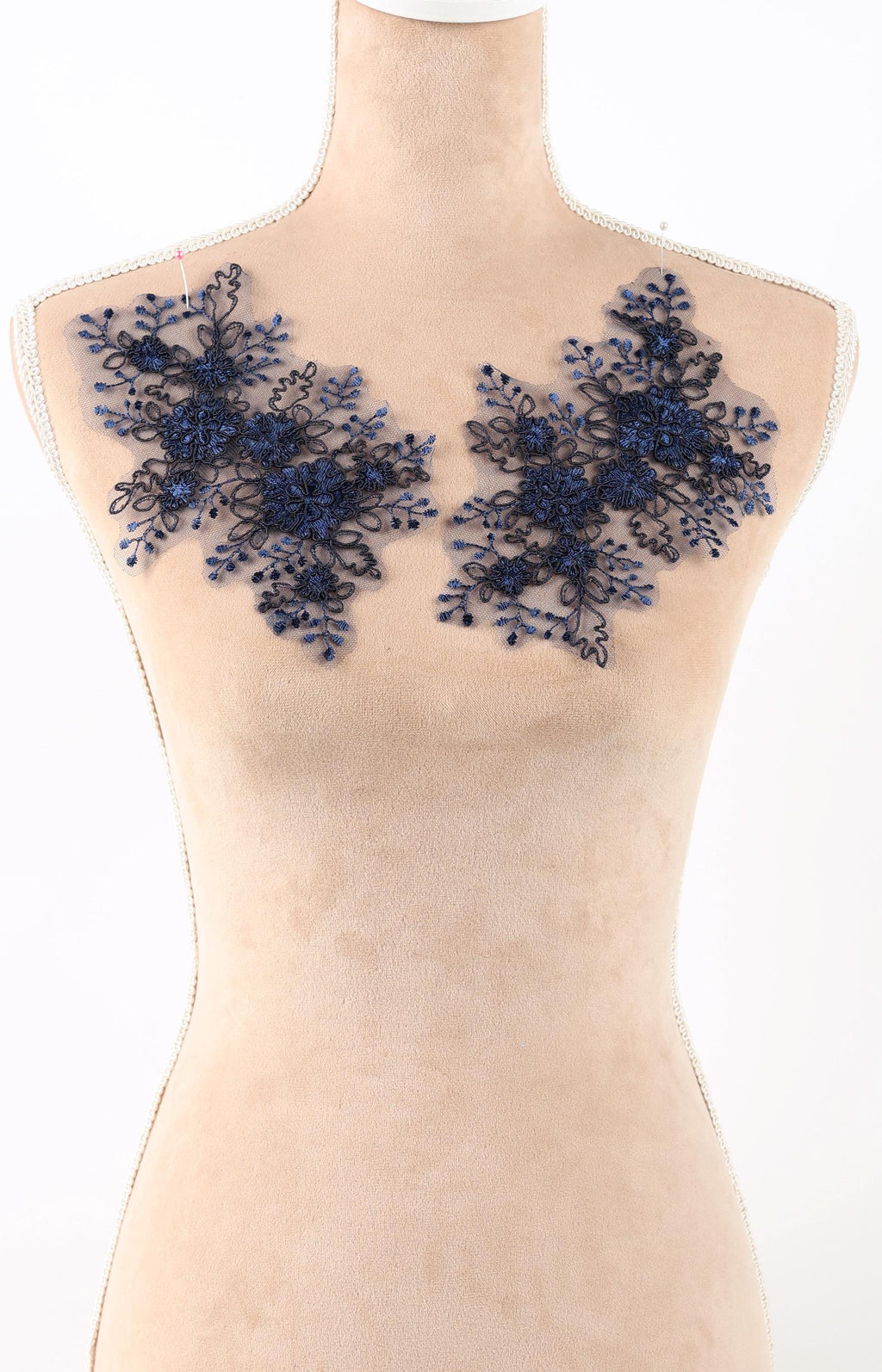 A mannequin wearing a beige dress with blue floral embroidery on the shoulders.