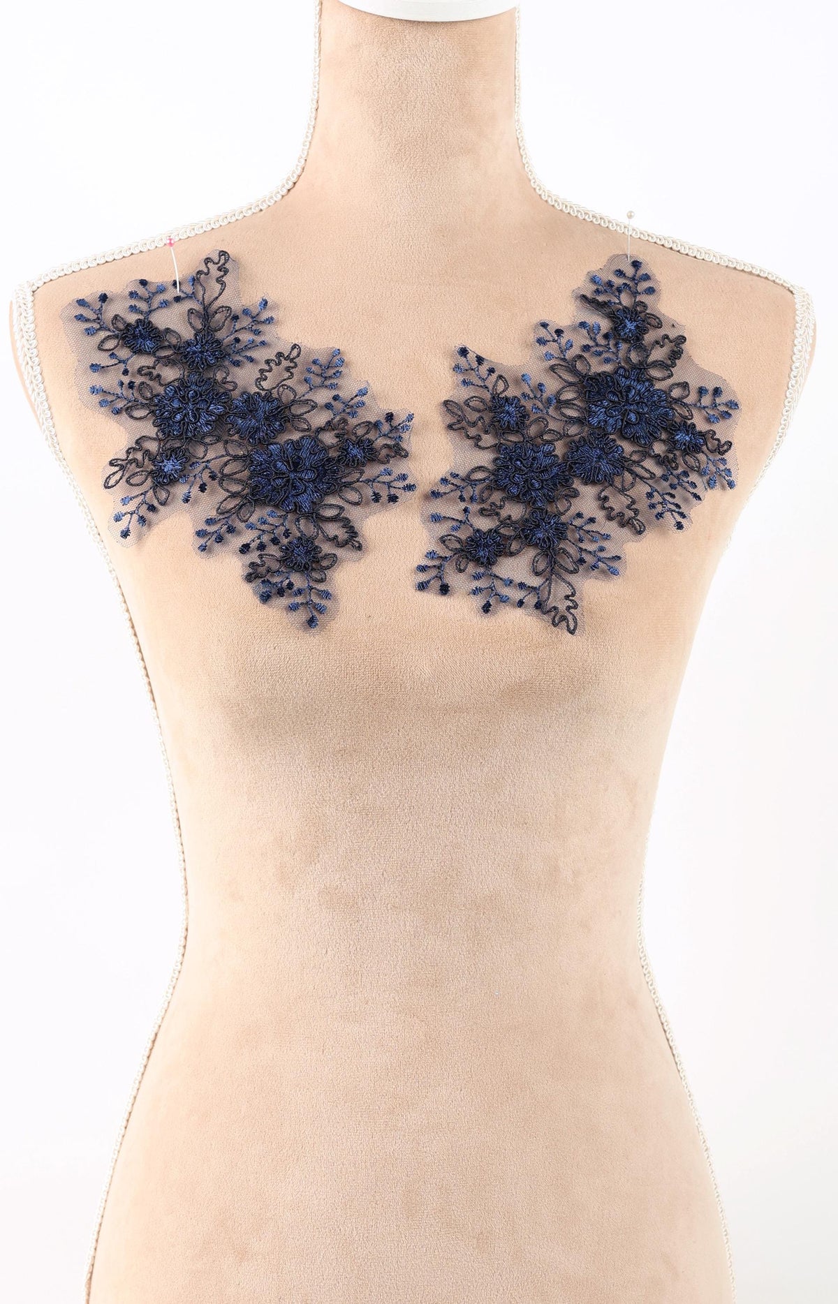 A mannequin wearing a beige dress with blue floral embroidery on the shoulders.