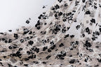 a close-up view of a fabric with a floral pattern, predominantly black and white. The fabric appears to be made of sheer material, with a delicate and intricate design of black flowers and leaves. The image does not contain any text or other discernible objects, and the focus is solely on the fabric and its floral pattern.