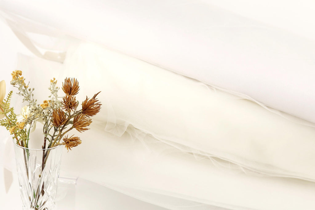 A clear glass vase filled with dried flowers sits on a white surface, accompanied by a white fabric or material.
