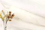 A clear glass vase filled with dried flowers sits on a white surface, accompanied by a white fabric or material.