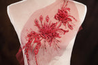 A mannequin wearing a dress with a red floral embellishment on the shoulder.