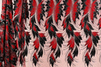 a close-up view of a fabric with a striking pattern of red and black feathers or leaves. The pattern is intricate and detailed, with the feathers or leaves appearing to be made of sequins or beads, adding a touch of sparkle to the design. The fabric is predominantly pink, providing a contrasting background for the bold red and black elements. The image does not contain any text or other discernible objects, and the focus is solely on the fabric and its captivating design.
