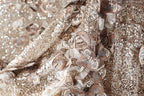 The image is a close-up of a fabric with a gold and brown color scheme, featuring intricate embroidered designs and sequins.