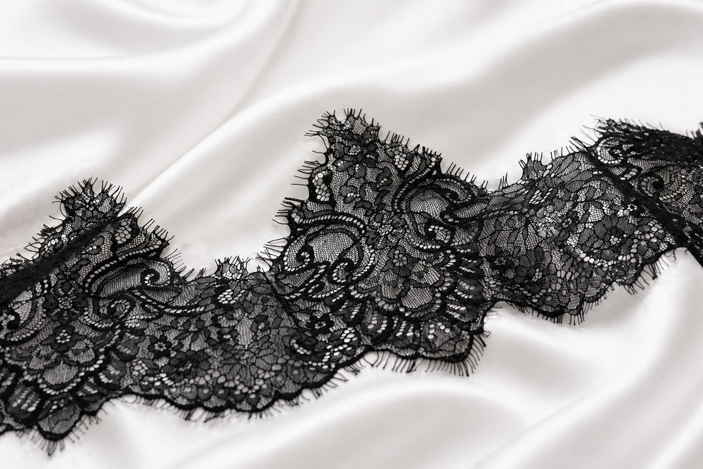 A close-up view of a delicate black lace trim on a white fabric surface.