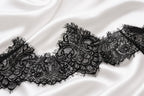 A close-up view of a delicate black lace trim on a white fabric surface.