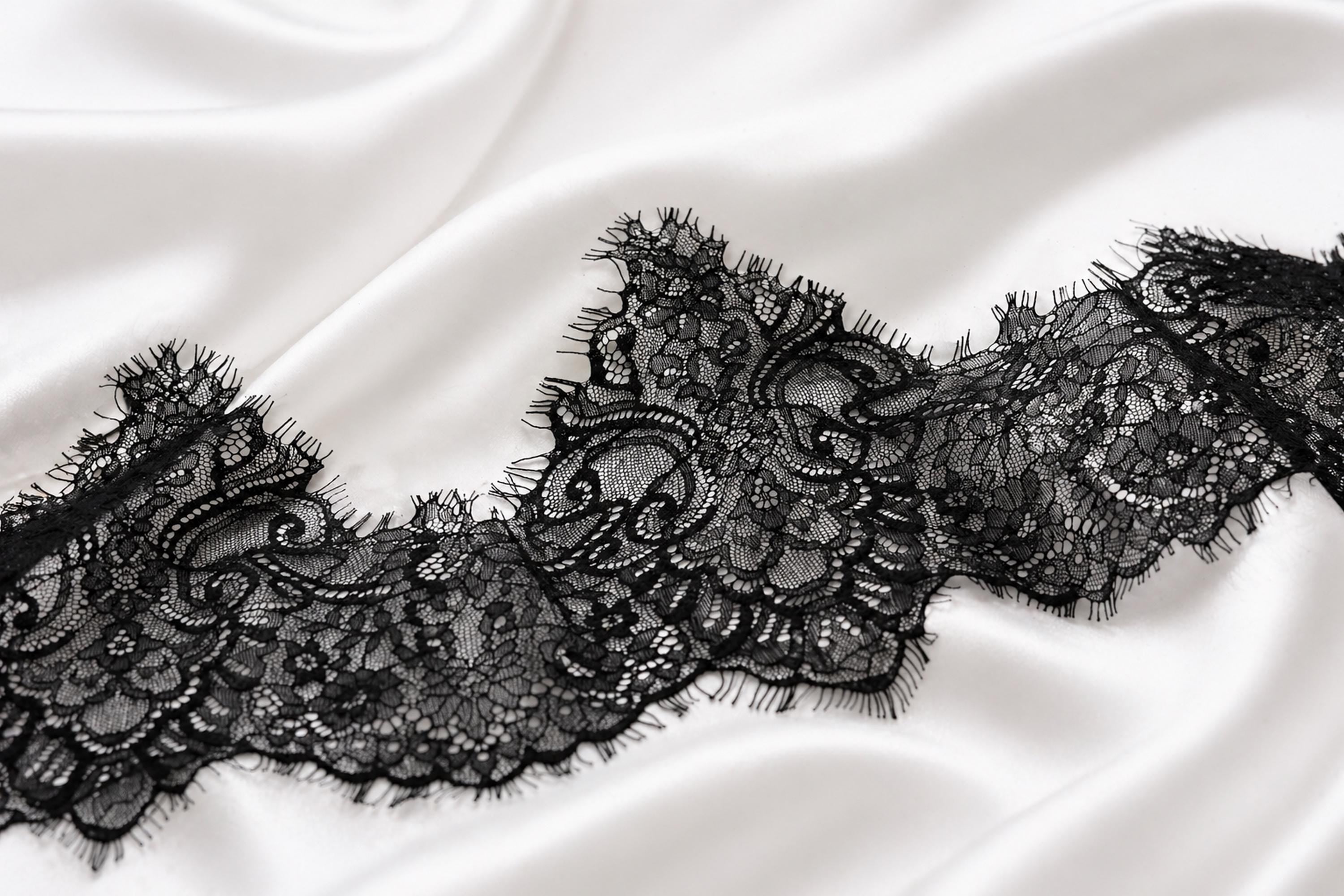 A close-up view of a delicate black lace trim on a white fabric surface.