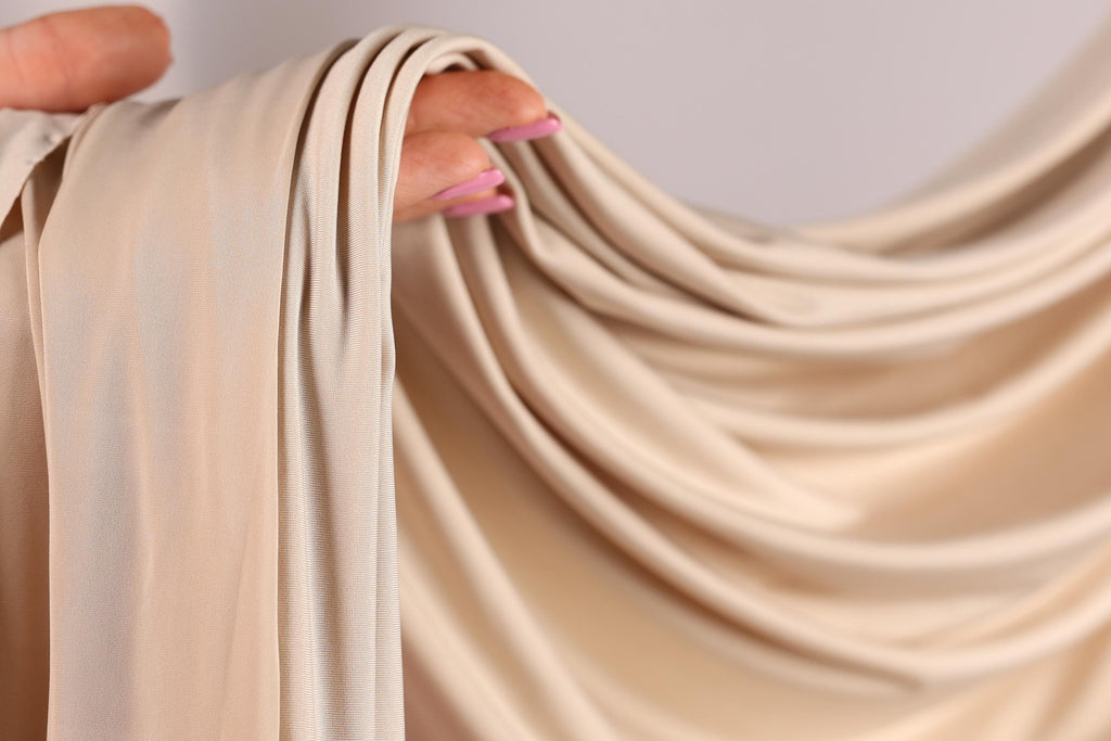 A hand holding a piece of light-colored fabric, possibly a sheer or sheer-like material, with the fingers curled around it.