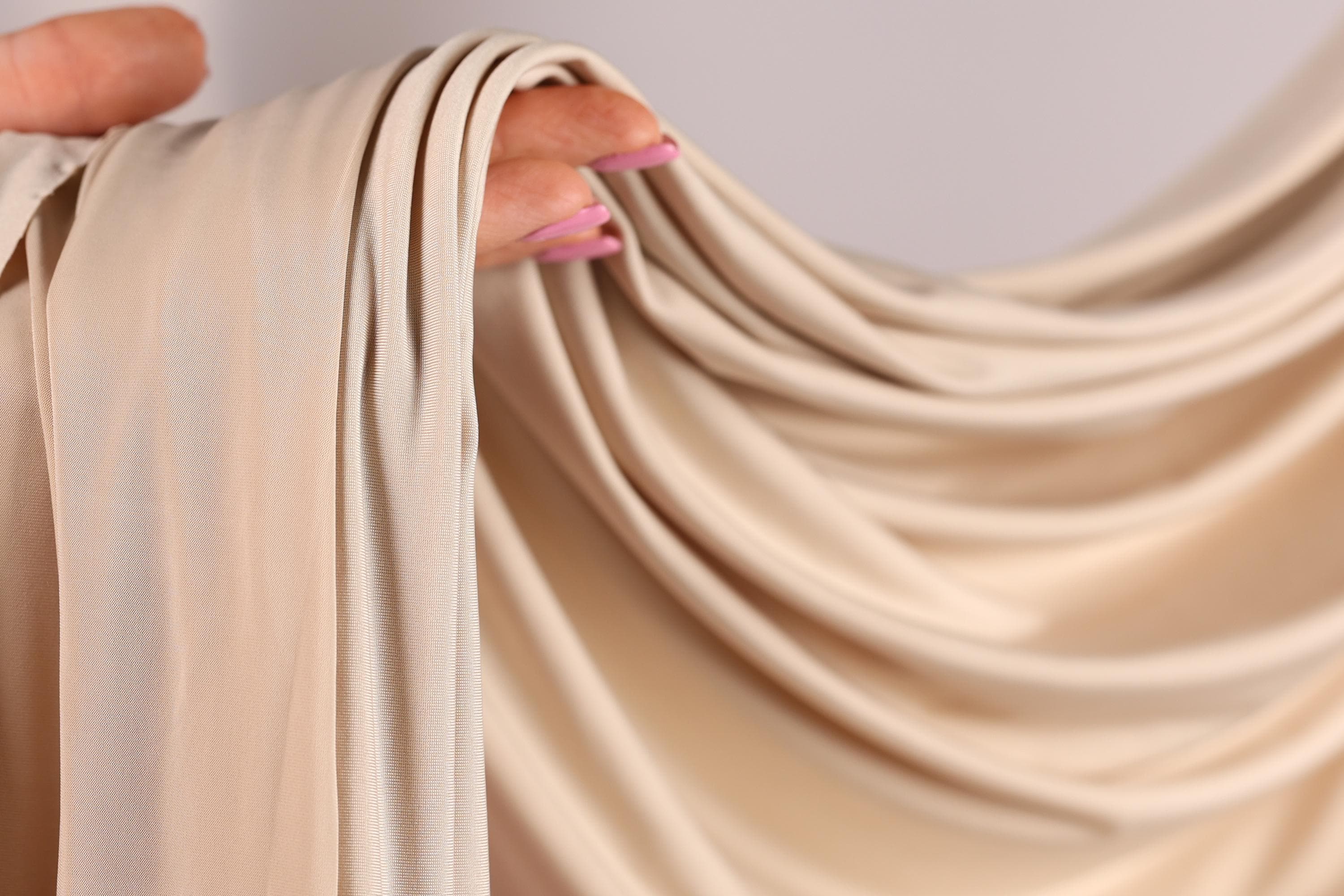 A hand holding a piece of light-colored fabric, possibly a sheer or sheer-like material, with the fingers curled around it.