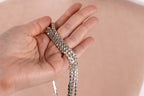 A hand holding a silver necklace with multiple small diamonds.