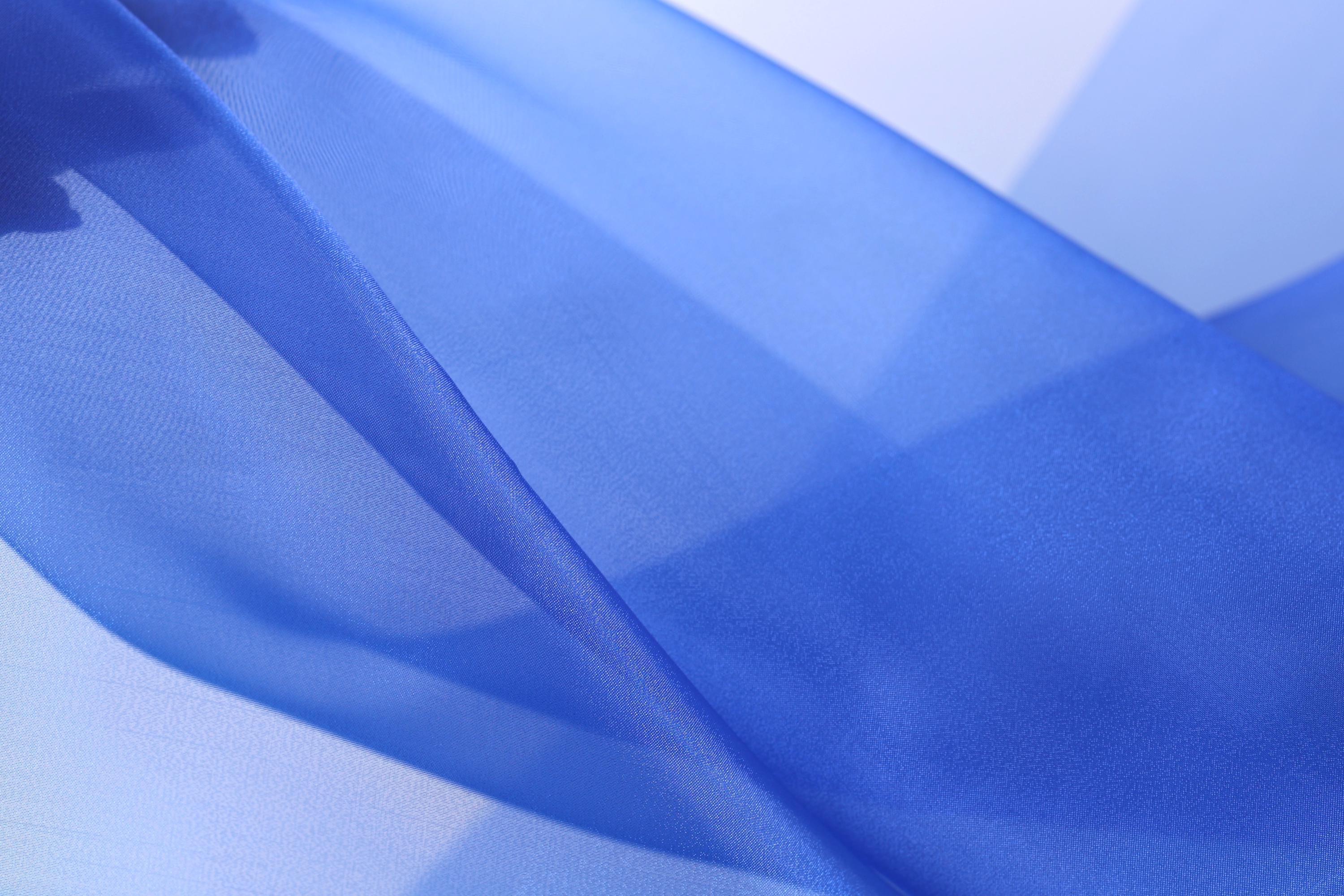 The image is a close-up of a blue fabric, possibly silk or chiffon, with a smooth and flowing texture.