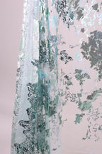The image is a close-up of a fabric with a pattern of green and silver sequins or glitter, creating a textured and visually striking appearance.
