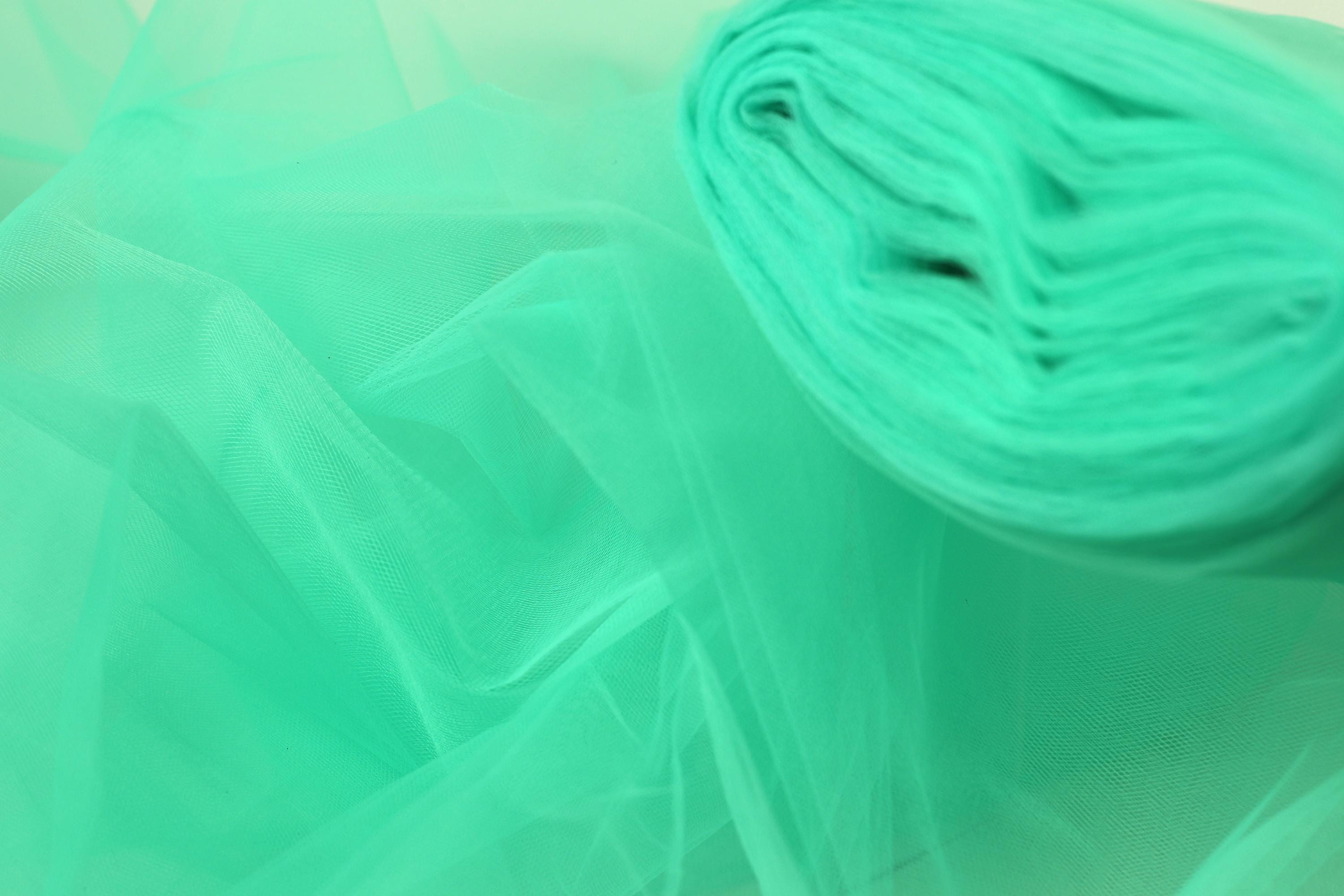 A close-up view of a piece of turquoise-colored fabric, possibly tulle, with a blurred green background.