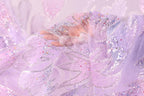 A hand is holding a piece of fabric with a delicate, sparkling pattern in shades of pink and purple.