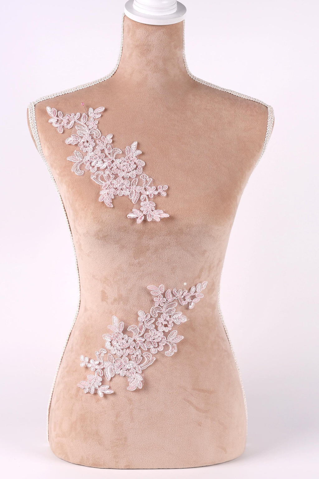 A mannequin with a beige body and a white head, adorned with delicate pink floral lace pieces on its torso.