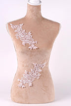 A mannequin with a beige body and a white head, adorned with delicate pink floral lace pieces on its torso.