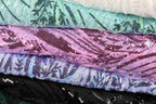 a close-up view of several colorful fabric pieces, including a purple and pink fabric with sequins, a white fabric with sequins, and a black fabric with sequins. The fabrics appear to be folded or stacked together, creating a visually appealing and textured composition.