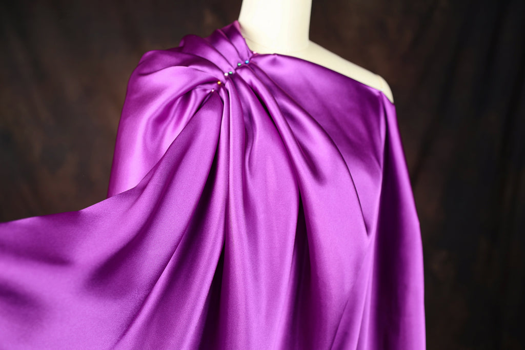 A mannequin wearing a vibrant purple satin dress with a draped, flowing silhouette.