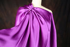 A mannequin wearing a vibrant purple satin dress with a draped, flowing silhouette.