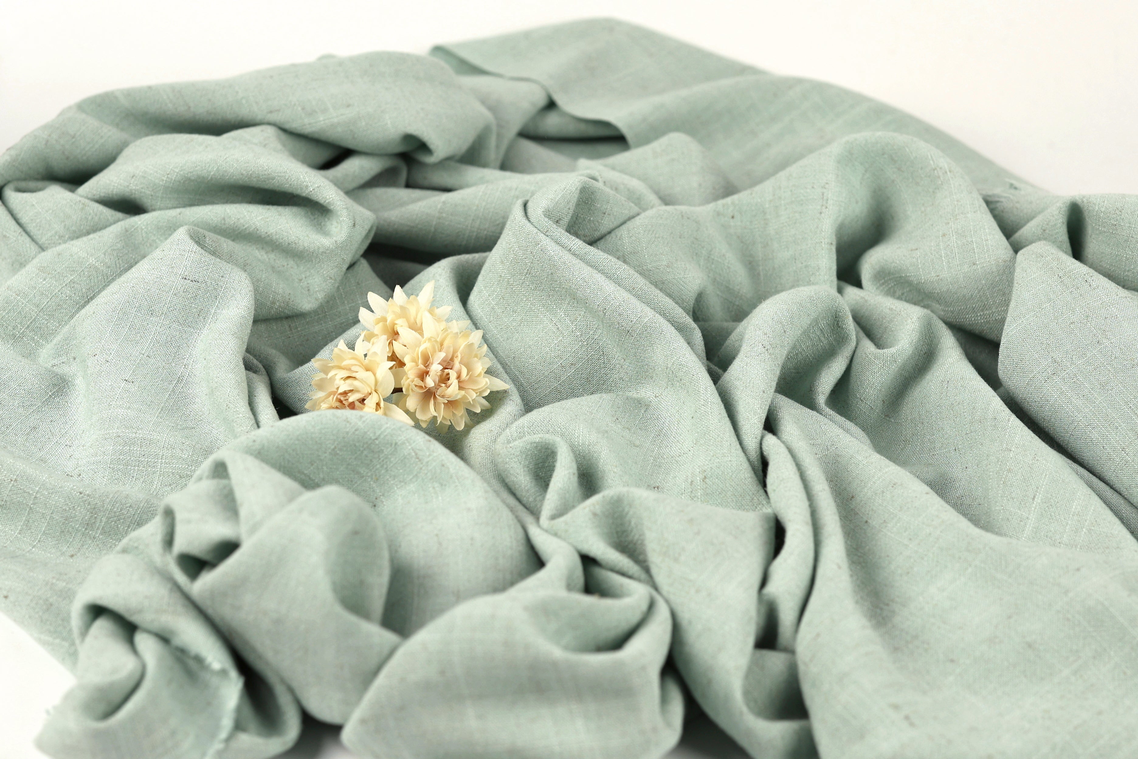 a close-up view of a crumpled light blue fabric with a single yellow flower resting on it.