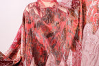 a close-up view of a vibrant, patterned fabric with a mix of red, pink, and orange colors. The fabric appears to be made of a shiny, sequined material, giving it a luxurious and eye-catching appearance.