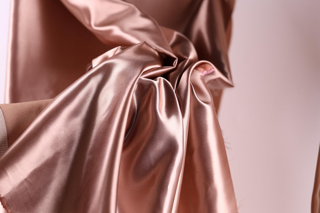 A close-up view of a crumpled, shiny pink satin fabric, with a blurred background.