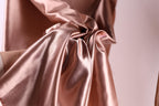 A close-up view of a crumpled, shiny pink satin fabric, with a blurred background.