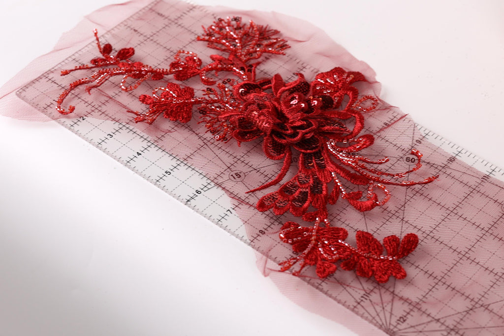 a close-up view of a red floral embroidery on a transparent surface, with a ruler placed on top of it.