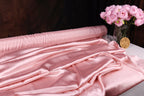 a pink satin fabric draped over a table, with a vase of pink flowers placed next to it.