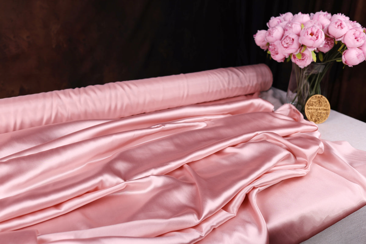 a pink satin fabric draped over a table, with a vase of pink flowers placed next to it.