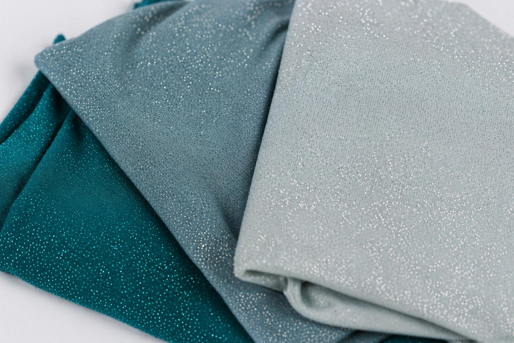a close-up view of three fabric swatches, each with a different color and texture. The swatches are arranged in a way that they overlap each other, creating a layered effect. The colors of the swatches are teal, blue, and gray, with the teal and blue colors being more prominent. The gray color is also visible in the image.