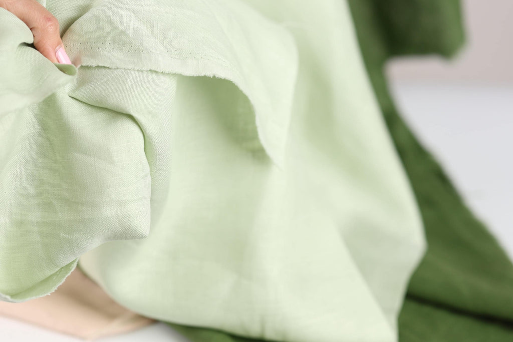 A close-up view of a fabric with a pale green color, partially overlapped by a darker green fabric.