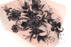 a close-up view of a delicate, intricate black lace design with numerous black flowers and leaves. The design is detailed and ornate, showcasing the craftsmanship and artistry involved in creating such a piece.