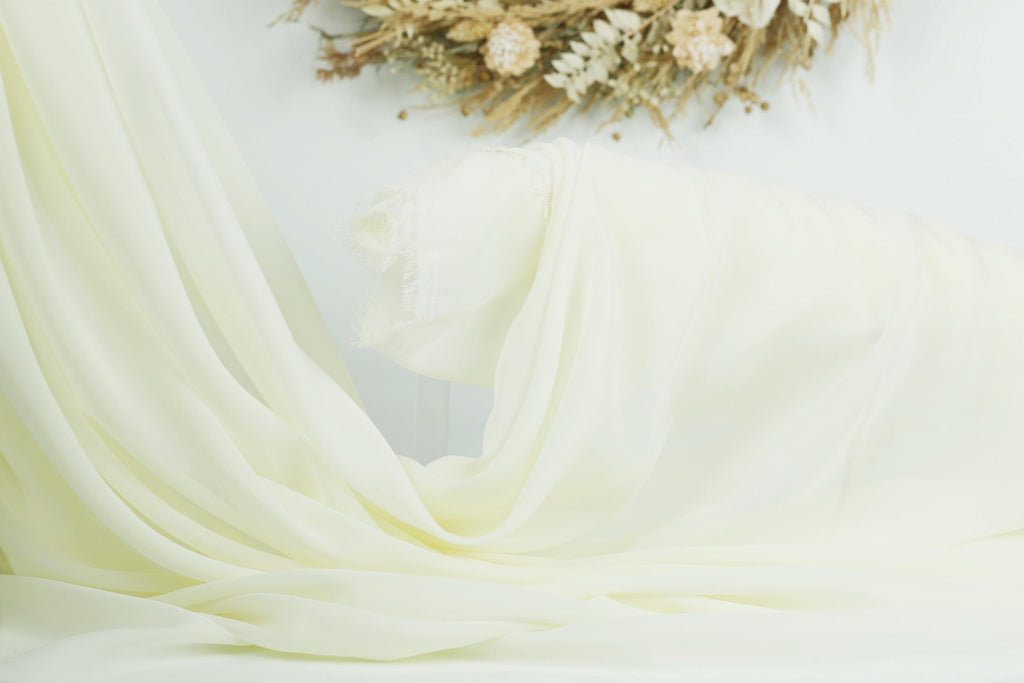 a white fabric draped over a surface, with a wreath of dried flowers in the background.