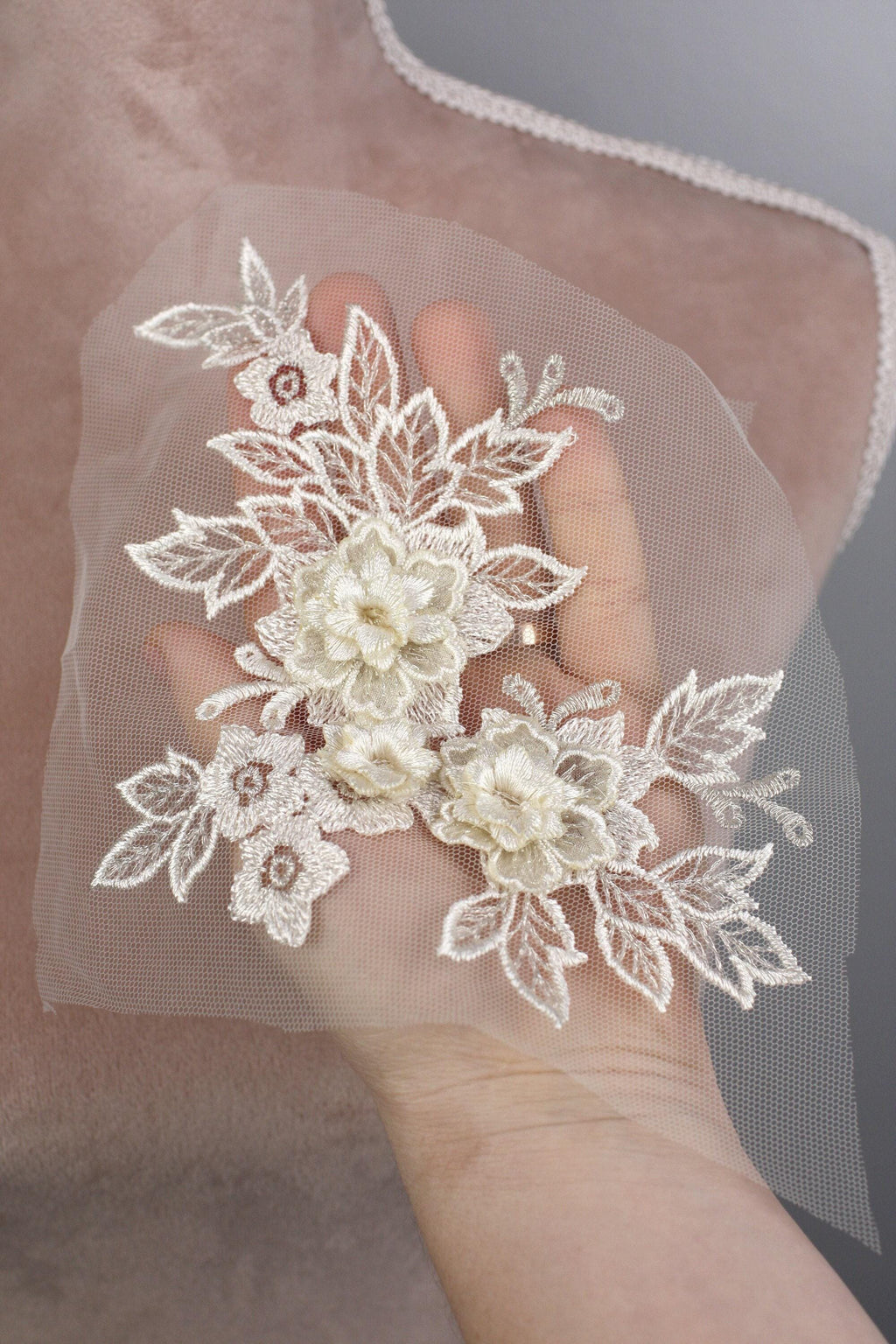 A hand holding a delicate white lace flower attached to a fabric.