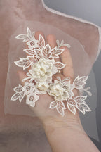 A hand holding a delicate white lace flower attached to a fabric.