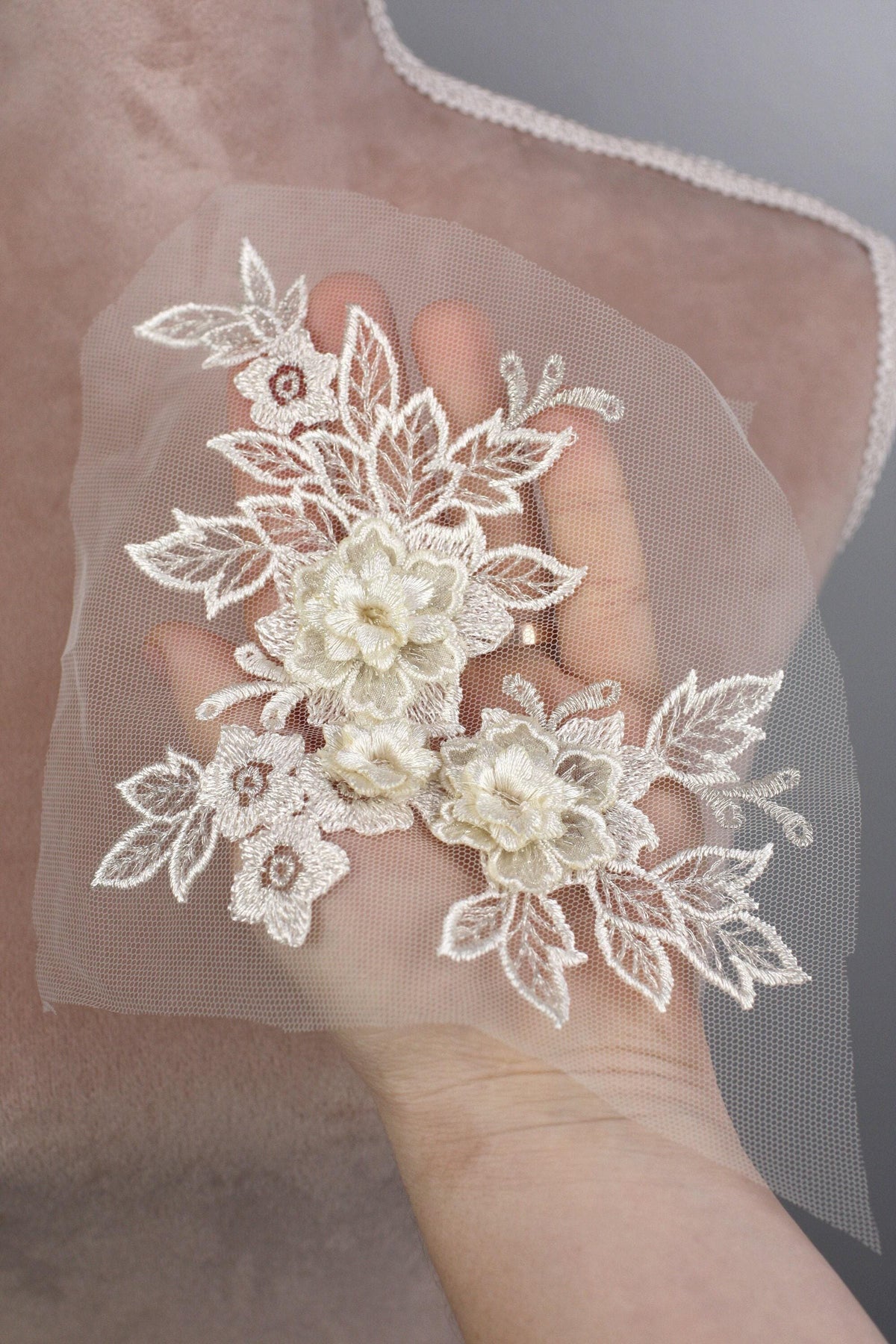 A hand holding a delicate white lace flower attached to a fabric.