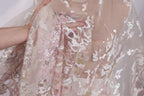 A close-up view of a delicate, lace-like fabric with a floral pattern, featuring a hand holding the fabric.