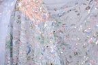 a close-up view of a delicate, intricately embroidered fabric with a floral pattern. The fabric appears to be made of sheer material, giving it a soft and delicate appearance. The embroidery features a variety of flowers and leaves, creating a visually appealing and detailed design. The fabric is spread out, allowing for a clear view of its intricate details and patterns.