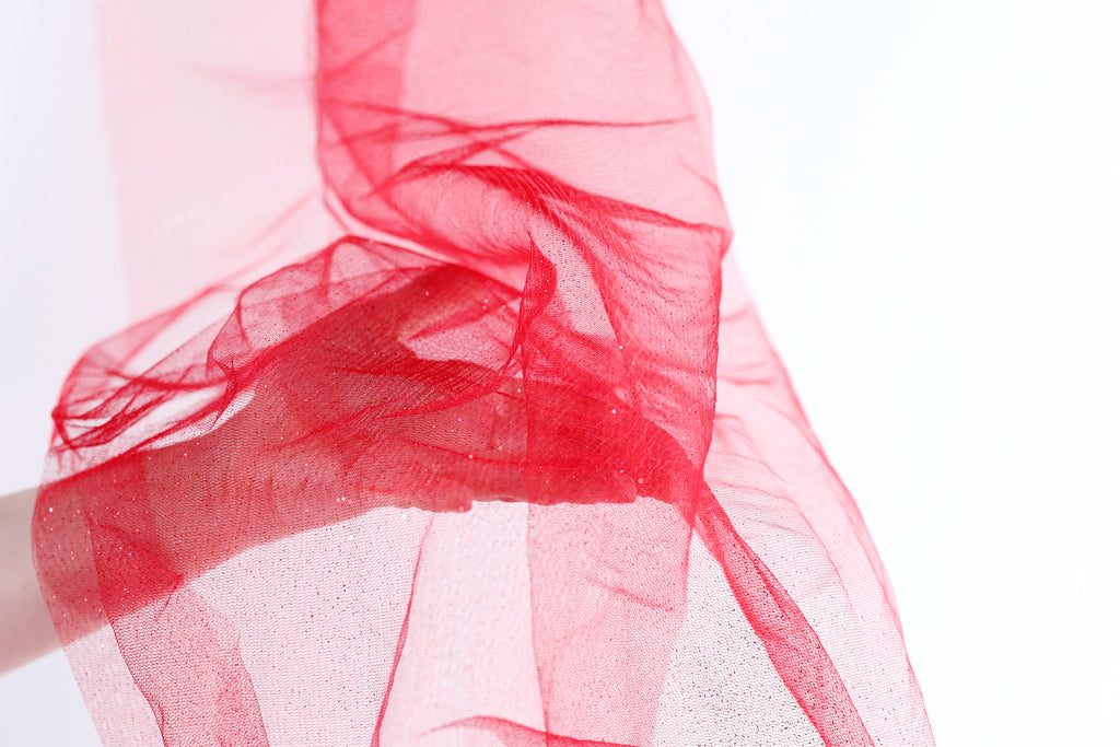 A hand is holding a red, flowing fabric that appears to be made of a sheer, translucent material.