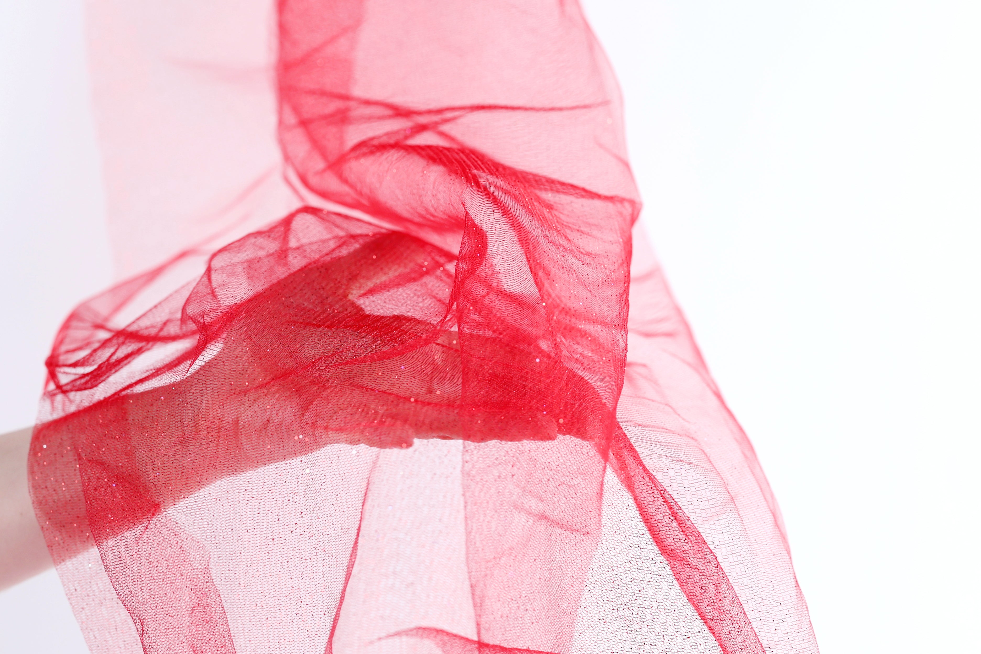 A hand is holding a red, flowing fabric that appears to be made of a sheer, translucent material.